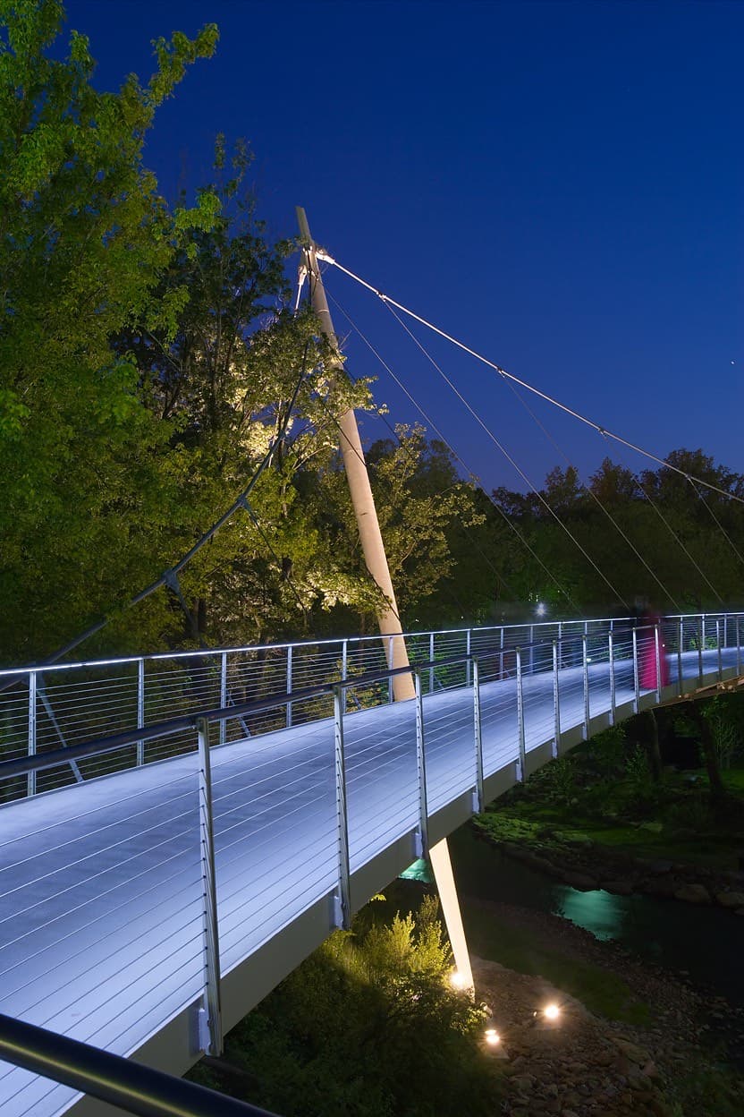 Liberty Bridge at Falls Park in Greenville, SC at night, with its lit curved deck and cable-supported mast